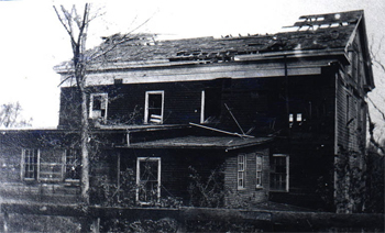 Black & white photo of wooden building with portion of roof missing