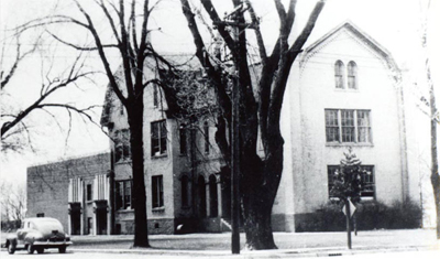 Black & white photo of three story building with one story addition in back